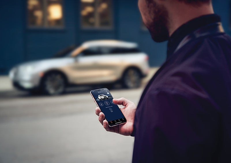 A person is shown interacting with a smartphone to connect to a Lincoln vehicle across the street. | Asheville Lincoln in Asheville NC