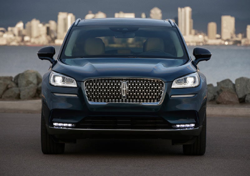 The front of a 2021 Lincoln Corsair in flight blue is illuminated with bright headlamps that cut through the dusk