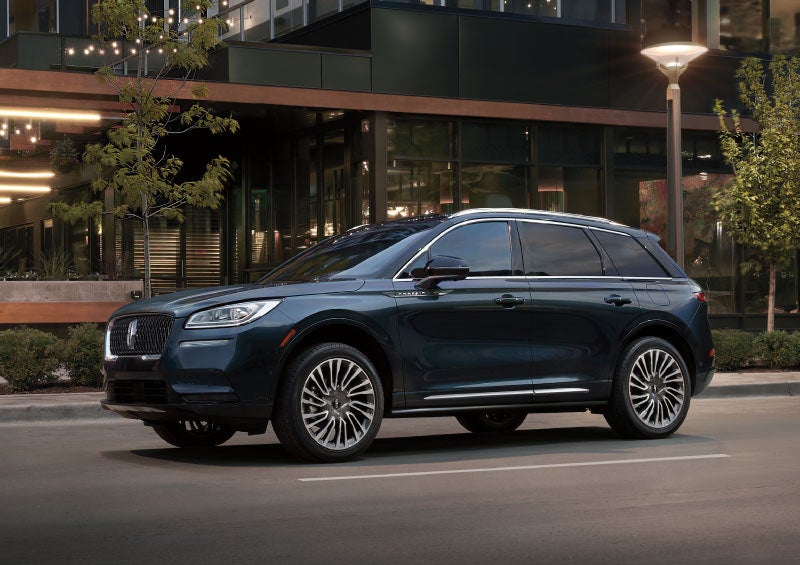 A 2021 Lincoln Corsair in Flight Blue is parked outside a downtown restaurant as the warm glow of city lights highlights the vehicles exterior form