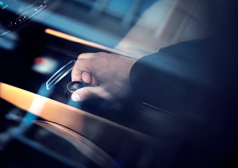 Through an exterior window reflecting surrounding skyscrapers we see a drivers hand turning the Lincoln drive modes knob near the center console