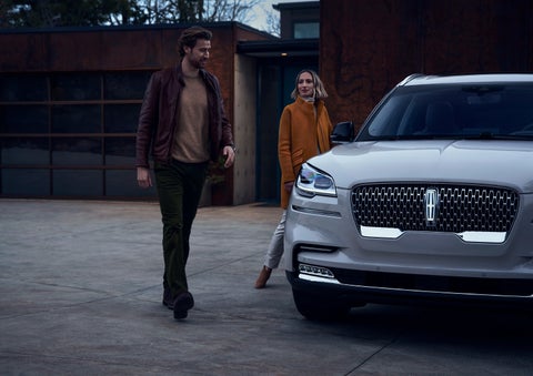 A man and a woman approaching a 2024 Lincoln Aviator® SUV, which illuminates certain lights when they are close | Asheville Lincoln in Asheville NC