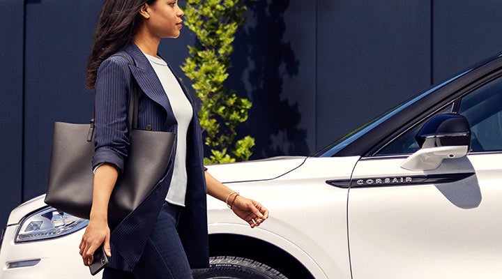 A woman approaches a 2024 Lincoln Corsair® SUV while holding a smartphone.