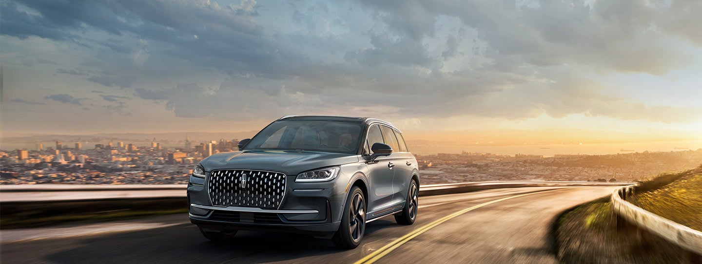 The 2024 Lincoln Corsair® Grand Touring SUV is driving on a road overlooking a city skyline.