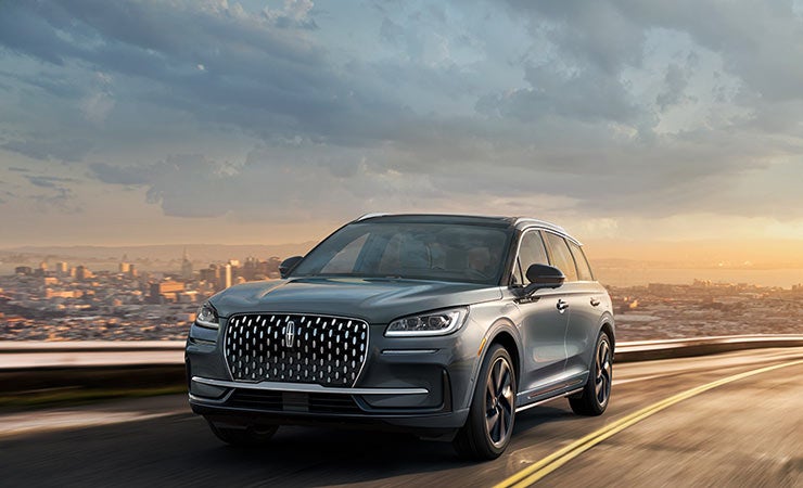 The 2024 Lincoln Corsair® Grand Touring SUV is driving on a road overlooking a city skyline.
