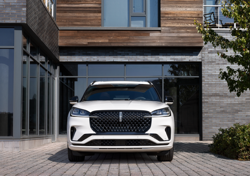 A white 2025 Lincoln Aviator® SUV is shown parked outside a modern building with gray brick and wood accents. | Asheville Lincoln in Asheville NC