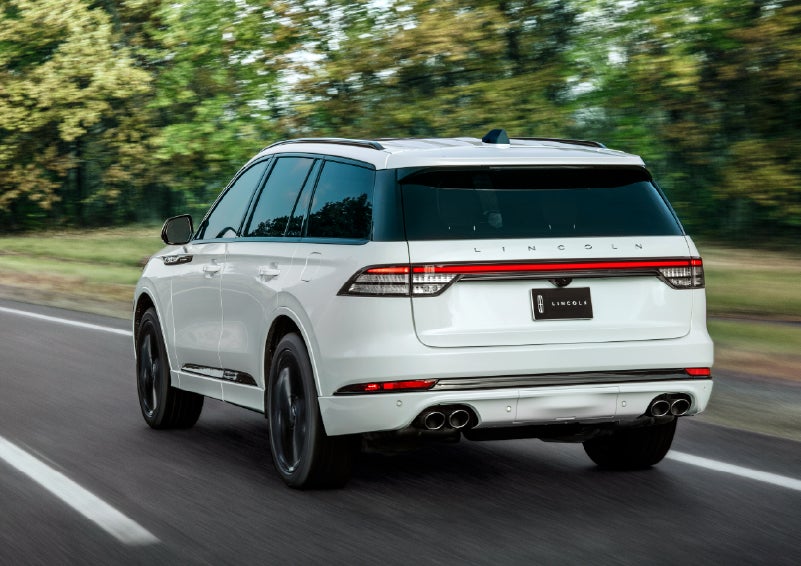A white 2026 Lincoln Aviator® SUV is being driven away down a road lined with colorful trees. | Asheville Lincoln in Asheville NC