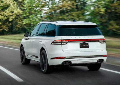 A white 2026 Lincoln Aviator® SUV is being driven away down a road lined with colorful trees. | Asheville Lincoln in Asheville NC