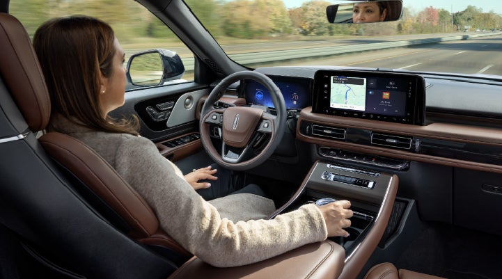 A 2027 Lincoln Aviator® SUV is being driven hands-free on a highway lined with trees. | Asheville Lincoln in Asheville NC