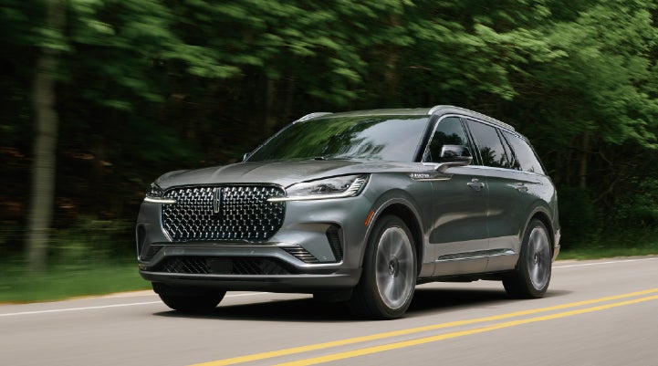 A 2027 Lincoln Aviator® SUV is being driven down a road lined with trees. | Asheville Lincoln in Asheville NC